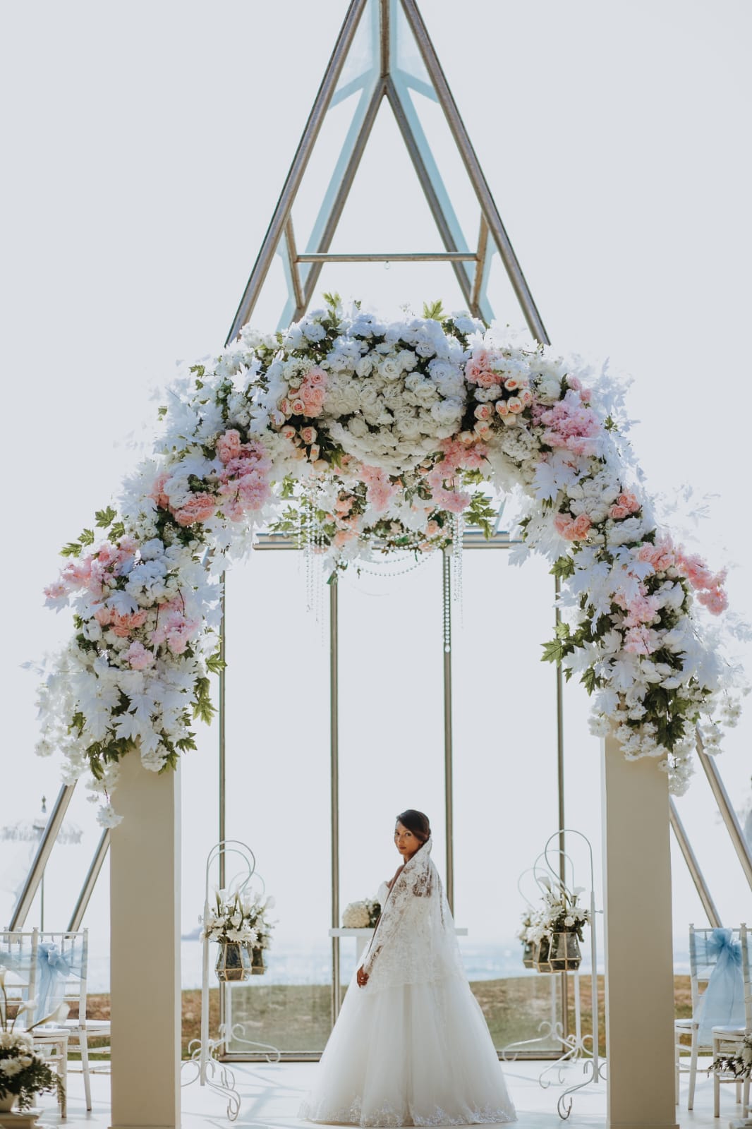 Bridal portrait in front of a glass chapel and floral arch