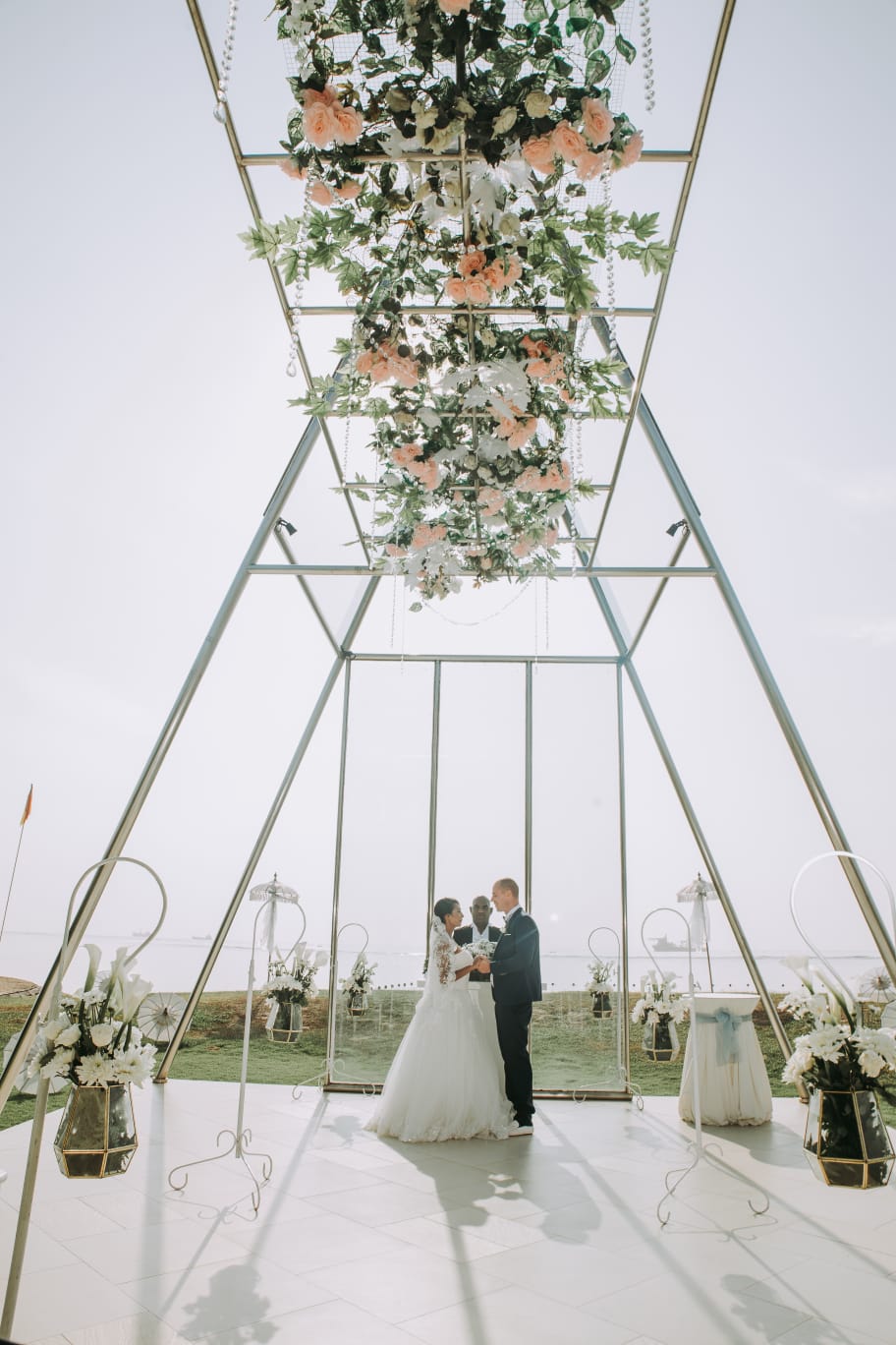 Couple exchanging vows inside a glass pavilion overlooking the sea